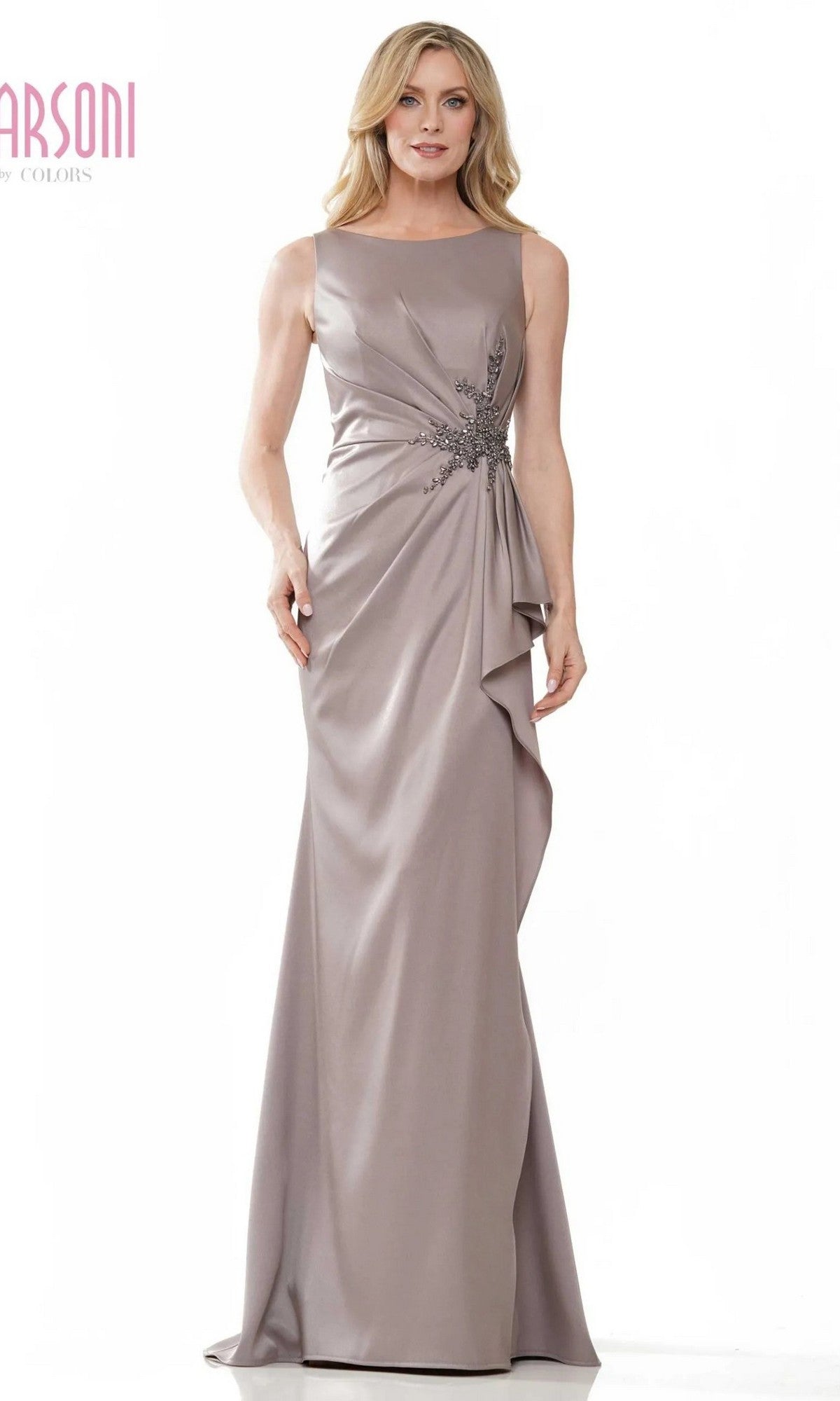 A woman in a sleeveless, floor-length taupe Marsoni MV1233 formal dress with side draping and floral waist embellishment stands against a white background.